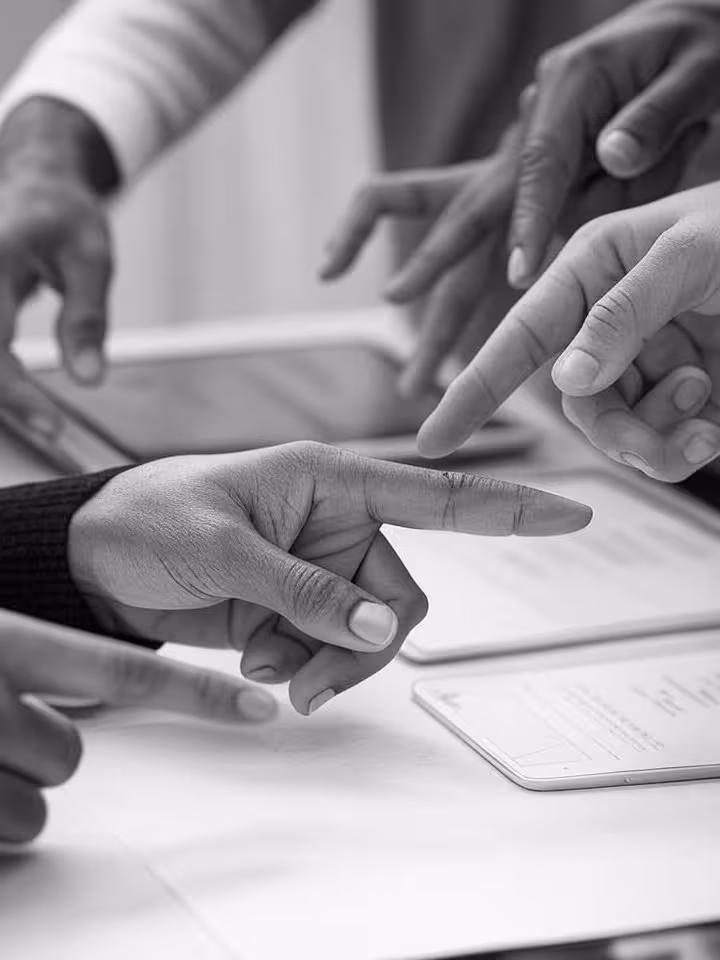 hands of designers from different cultures pointing at UI wireframes on tablets and paper prototypes